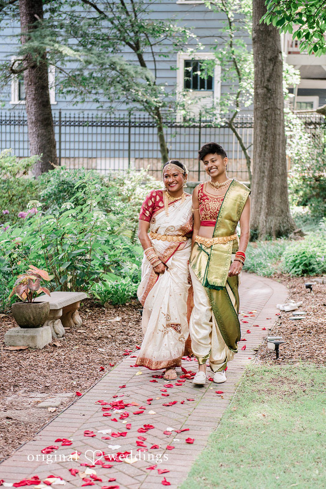 Sonya + Akshaya A couple walking together on a stone pathway scattered with red flower petals.
