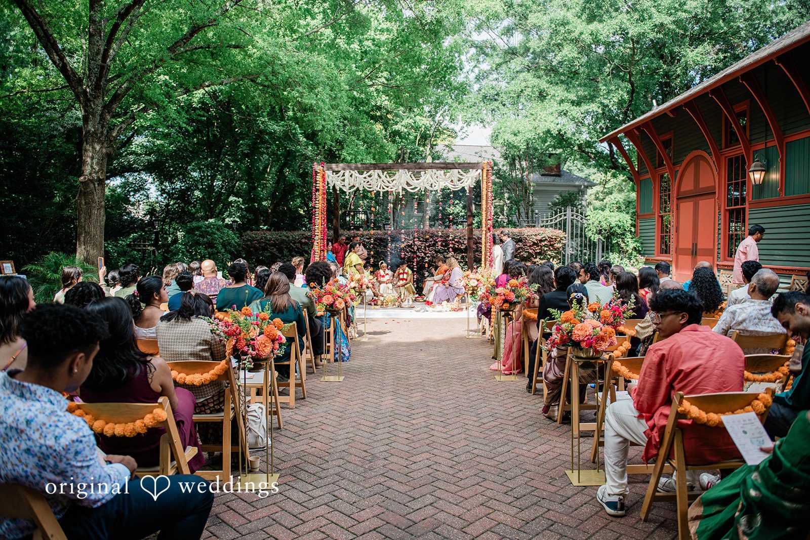 Sonya + Akshaya Seated guests watching a traditional wedding ceremony under a canopy of trees.