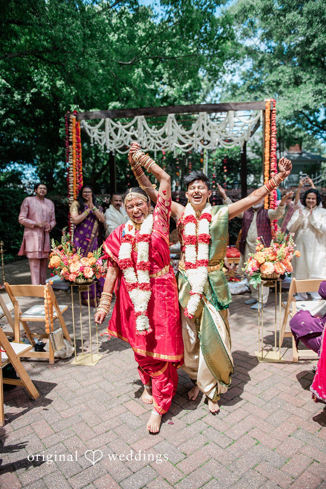 Sonya + Akshaya A couple walking joyfully down the wedding aisle with arms raised in celebration.
