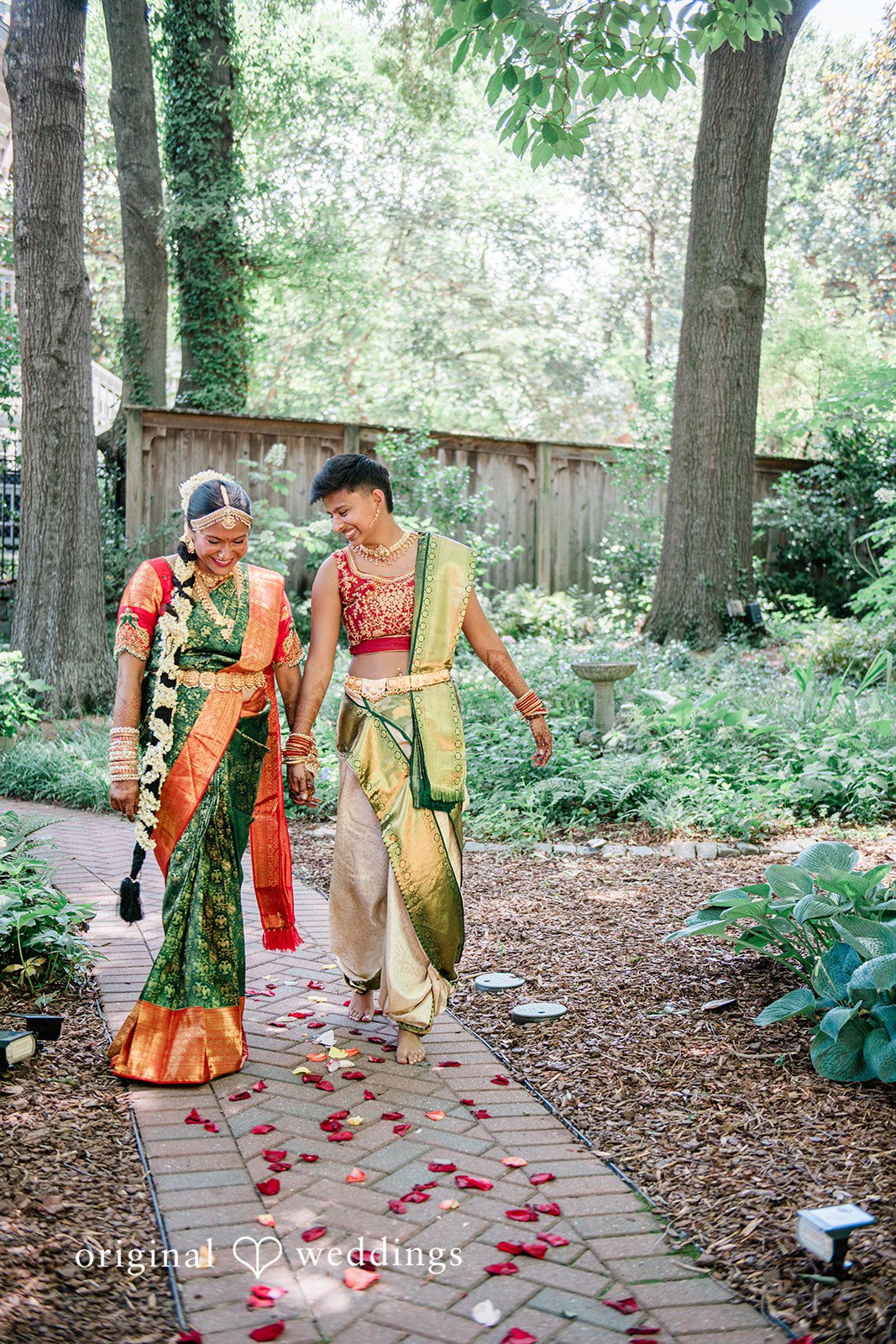 Sonya + Akshaya A couple walking hand-in-hand down a stone path lined with trees.