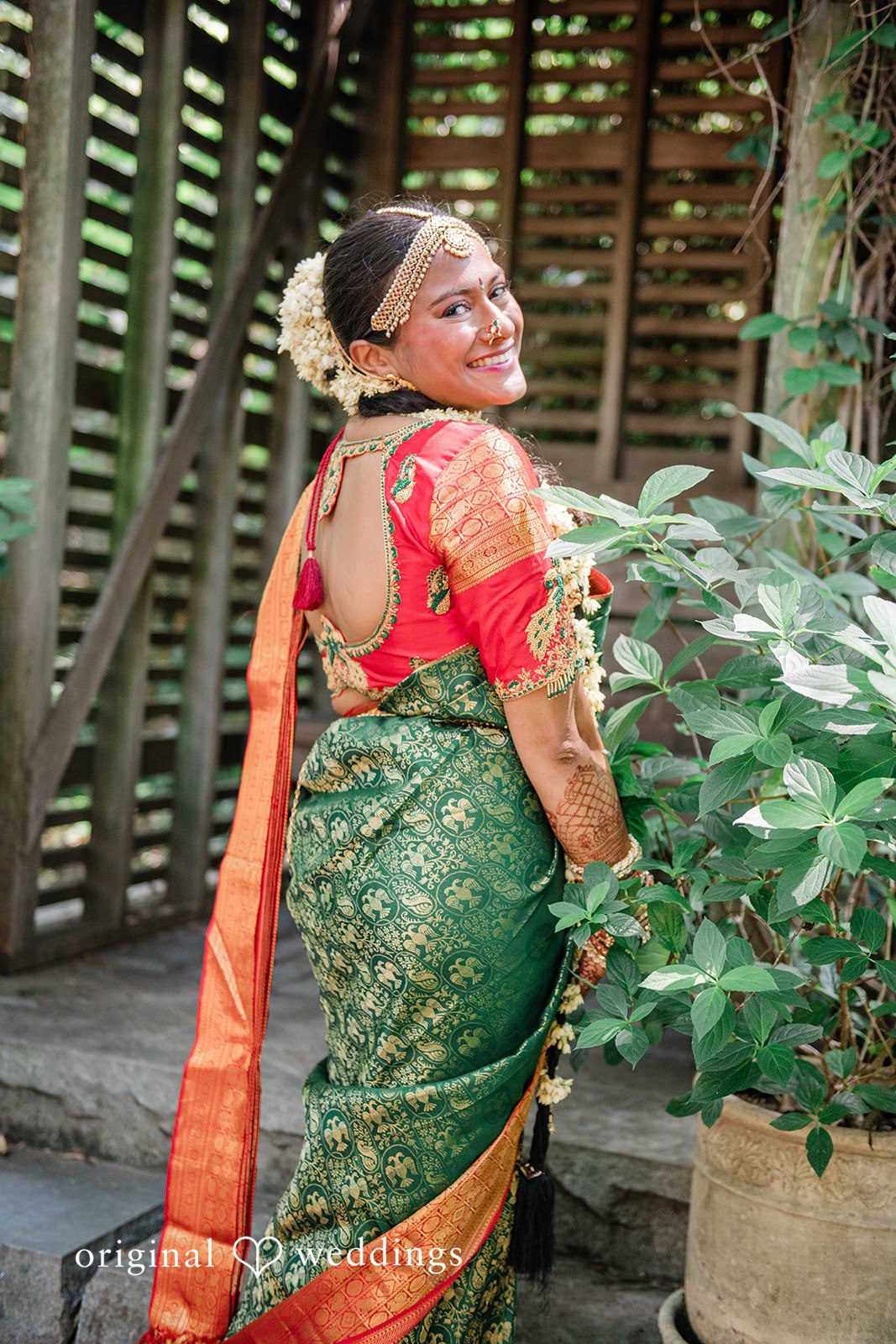 Sonya + Akshaya A bride looking back over her shoulder while wearing a green and orange saree.
