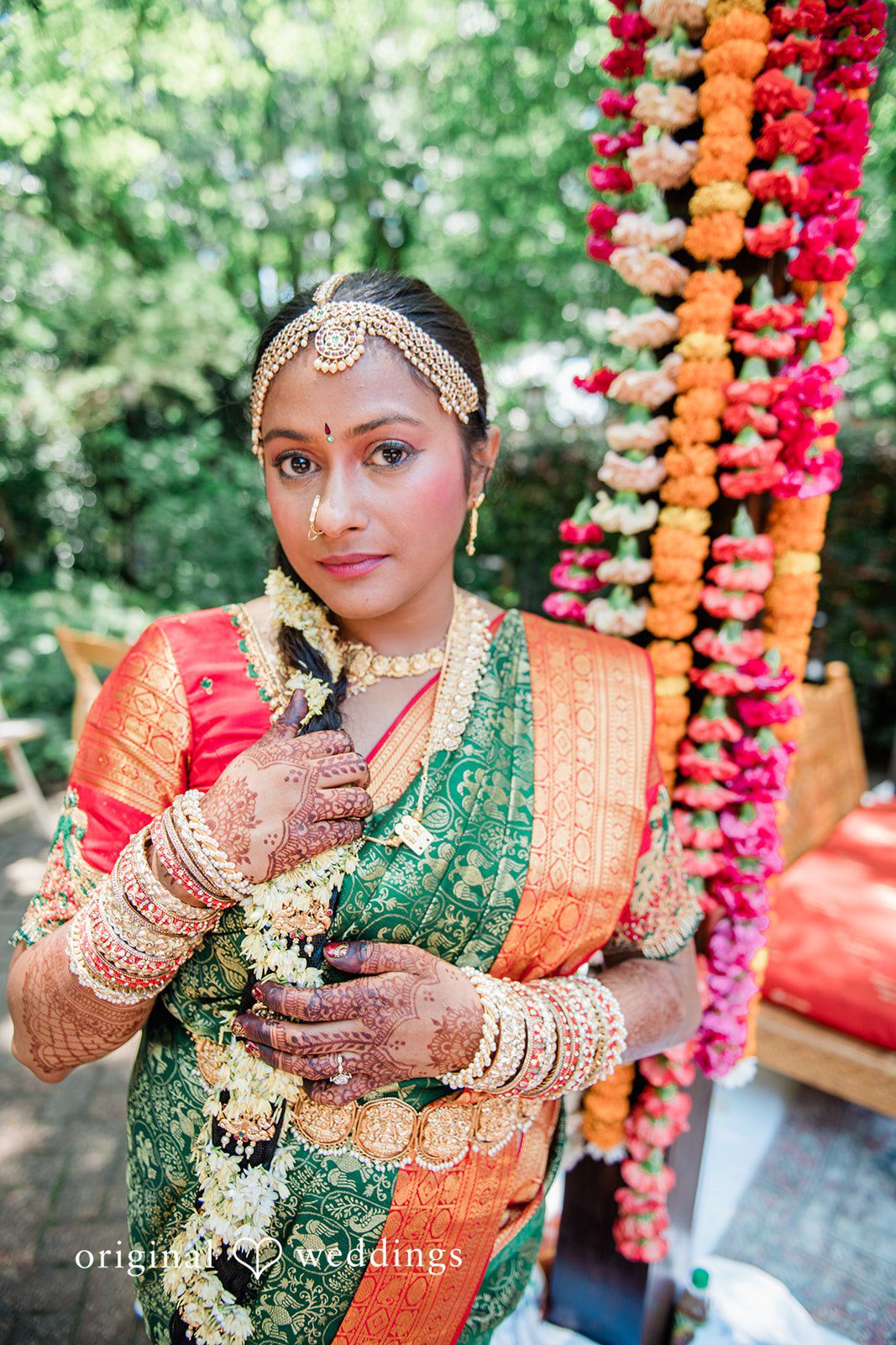 Sonya + Akshaya A bride posing elegantly in front of a backdrop of hanging flower garlands.