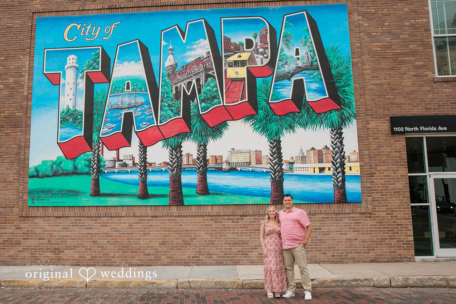 Taylor + Jack A couple standing in front of a large, vibrant, colorful painted mural on a brick wall.