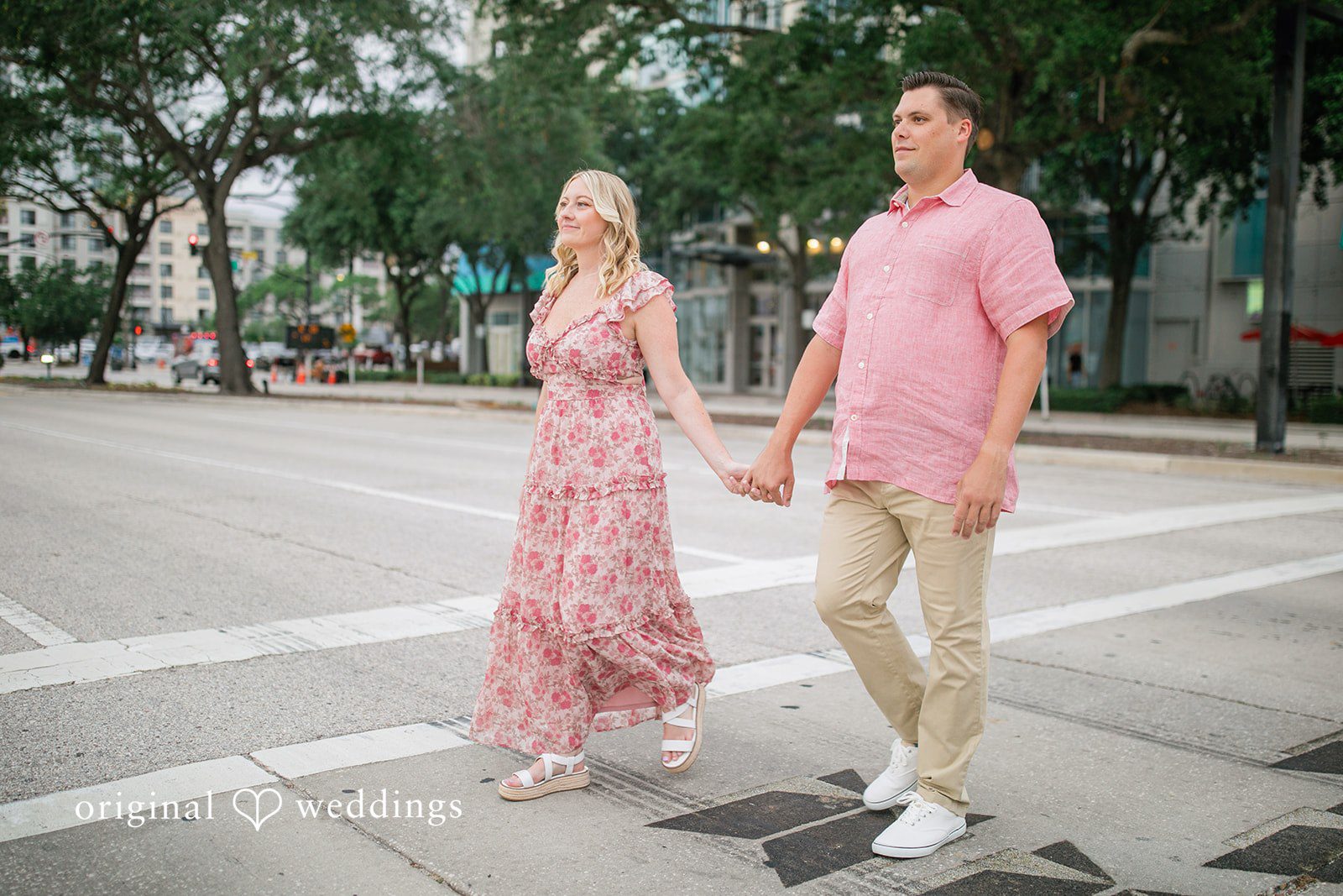 Taylor + Jack Couple holding hands and walking along a city sidewalk, both dressed in coordinated pink outfits.