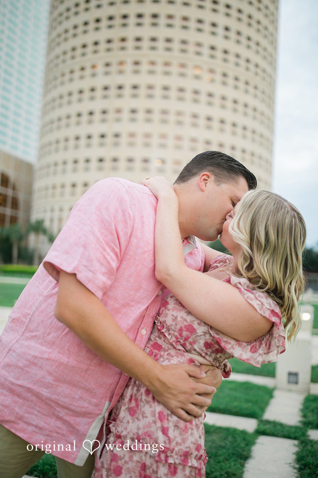 Taylor + Jack Man kissing a woman with a tall cylindrical skyscraper behind them.