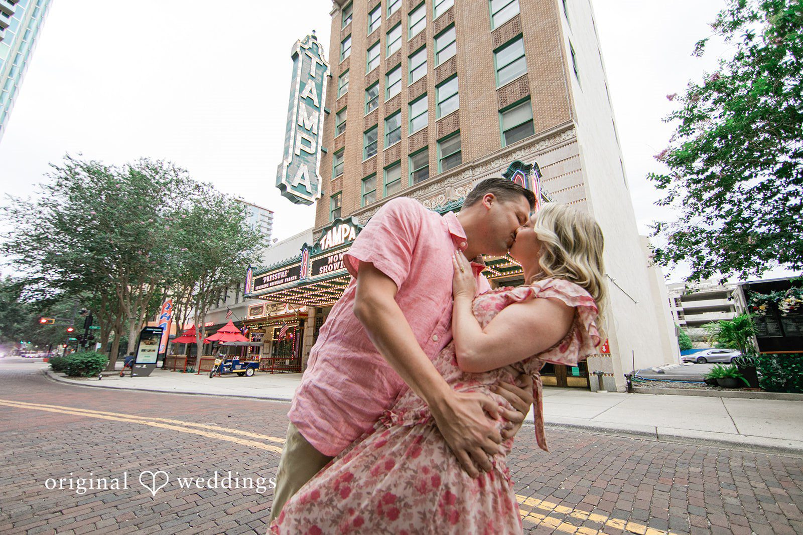 Taylor + Jack A man lifting and kissing a woman in a pink floral maxi dress on a city street.