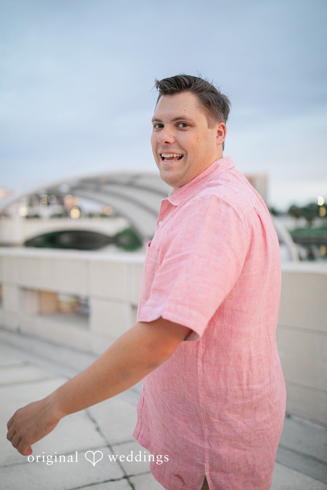 Taylor + Jack A man wearing a pink short-sleeved button-down shirt and smiling.