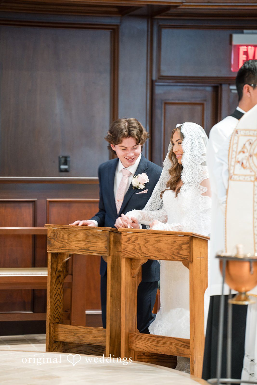Maya + Max A bride and groom sitting or kneeling at a wooden prayer desk during their church wedding ceremony