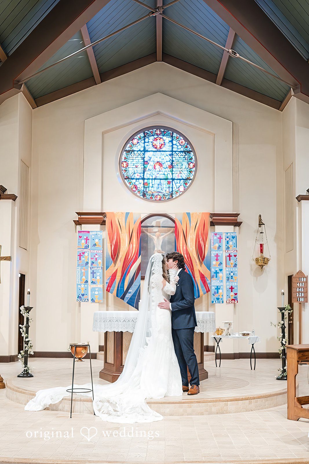 Maya + Max bride and groom sharing a kiss at the altar in front of a large colorful backdrop during their ceremony.