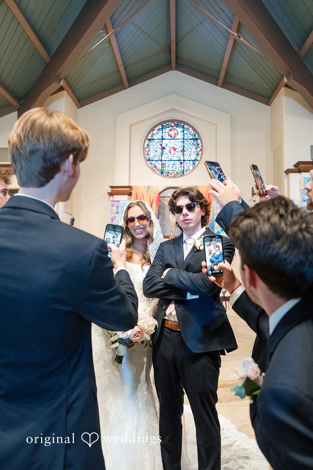 Maya + Max A couple wearing sunglasses and smiling while surrounded by wedding guests celebrating.