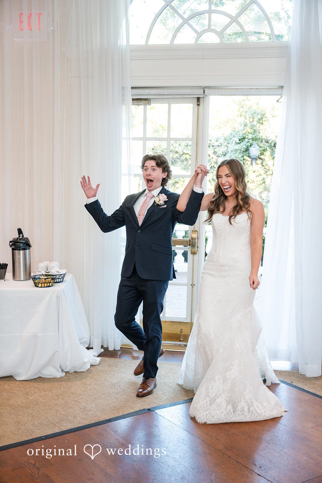Maya + Max A bride and groom making a grand entrance into their wedding reception with upraised hands.