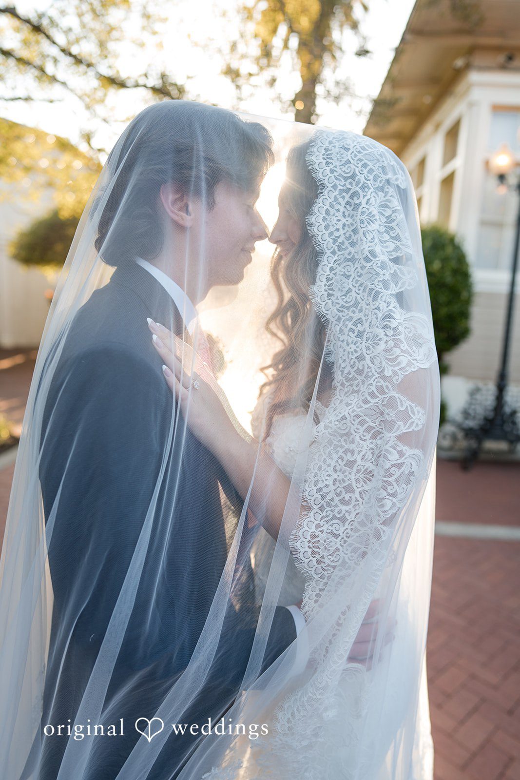Maya + Max A bride and groom looking into each other's eyes while wrapped together under a long wedding veil.