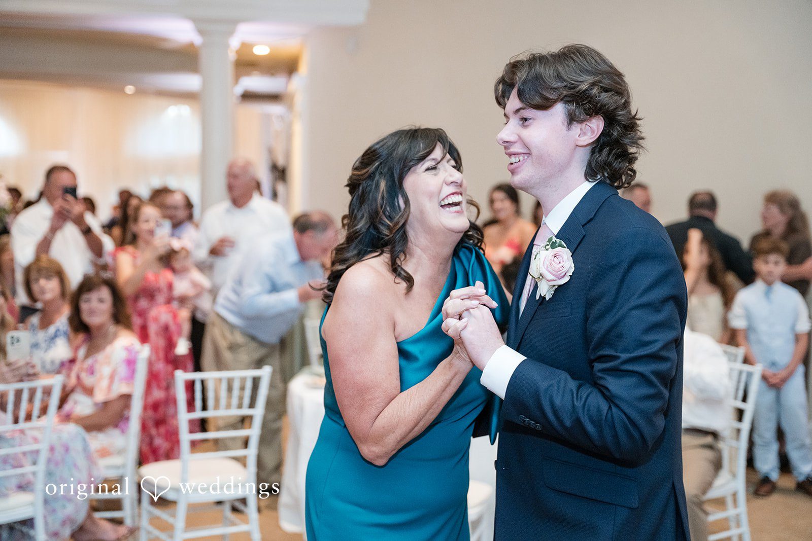 Maya + Max Groom smiling and dancing with a woman in a teal dress while guests watch.