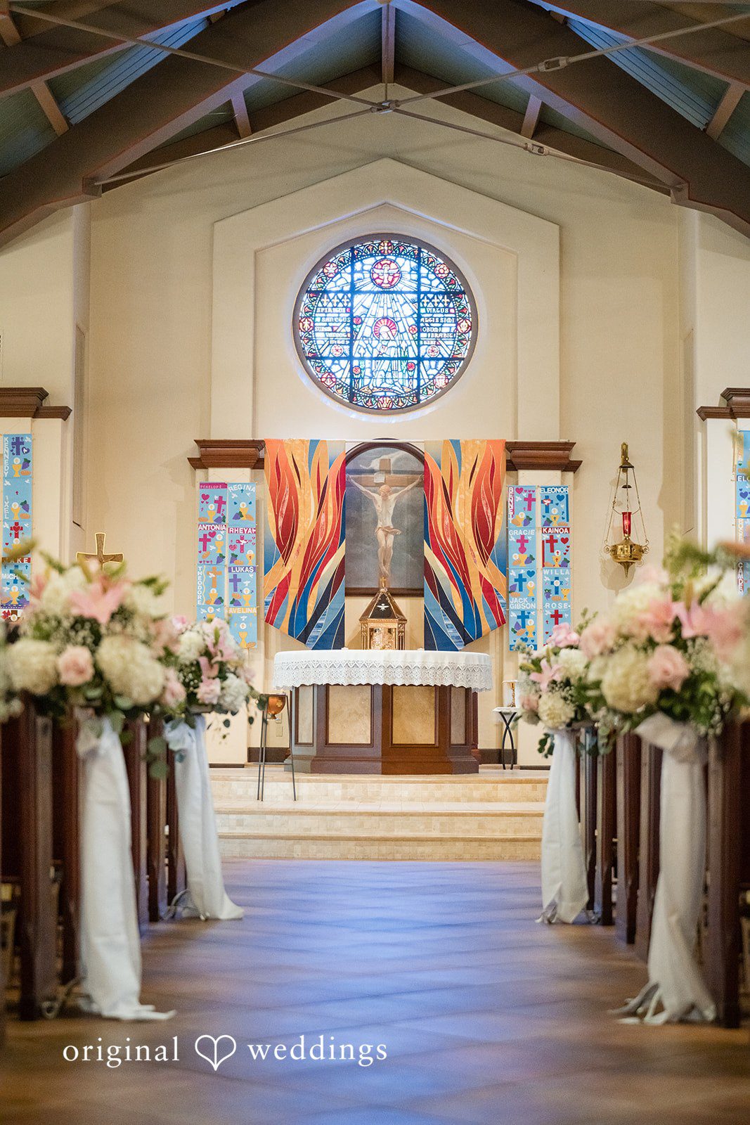 Maya + Max A church altar decorated for a wedding ceremony with floral arrangements lining the wooden pews and the center aisle.