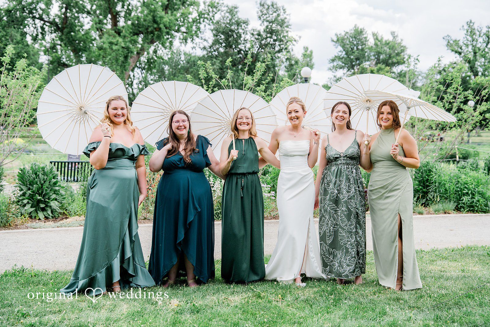 Sophia + Miles Bridesmaids wearing shades of green dresses posing while holding white paper parasols.