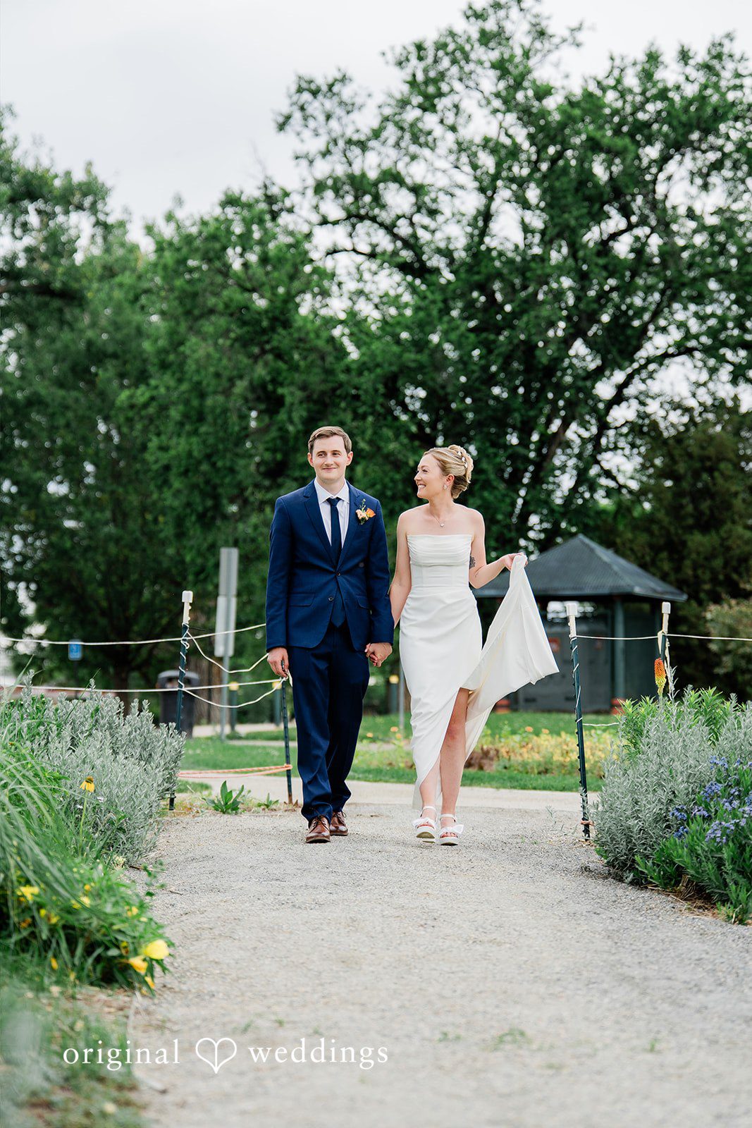 Sophia + Miles A bride and groom holding hands while walking along a stone walkway.