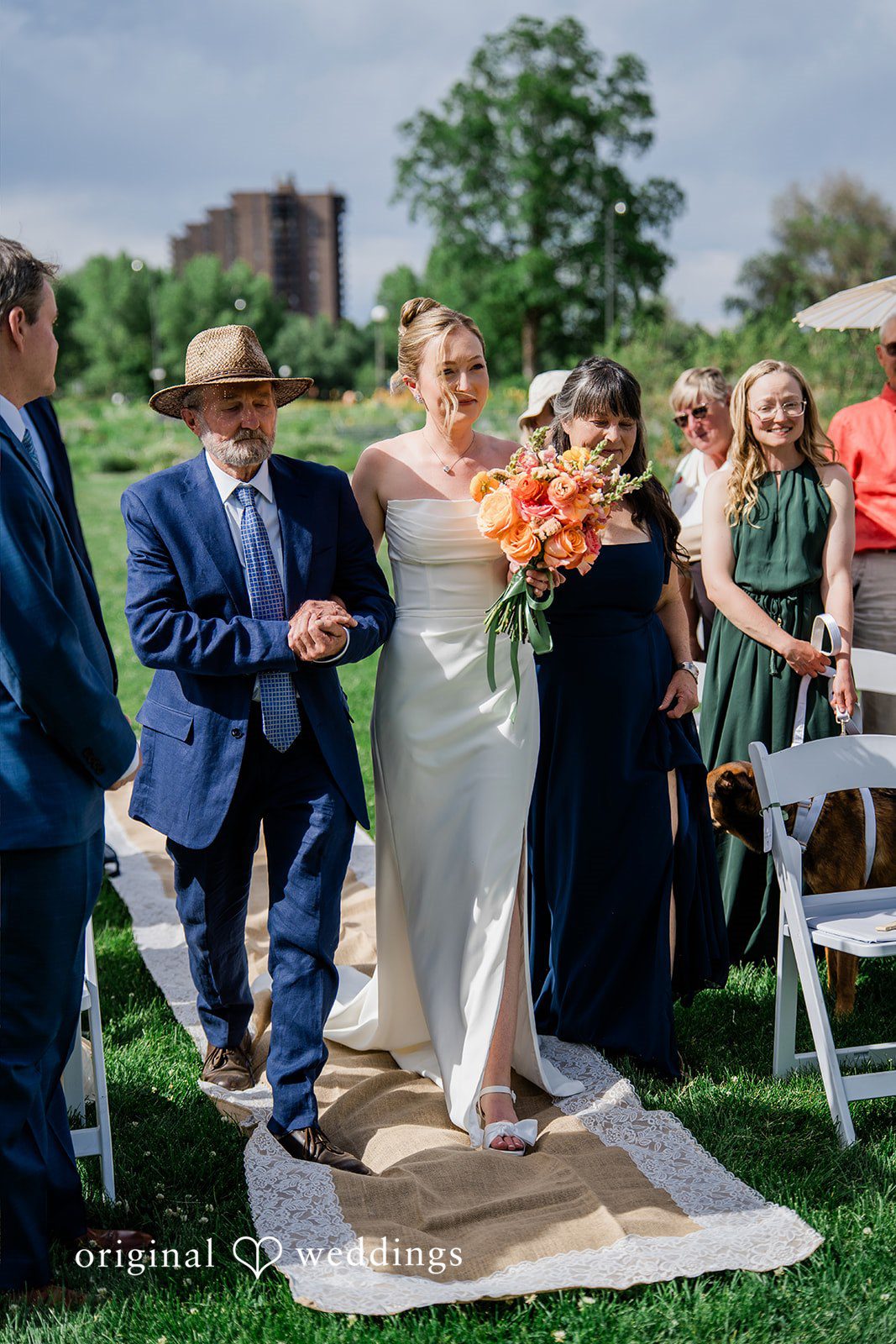 Sophia + Miles A newlywed couple walking down a grassy wedding aisle while guests watch and applaud.