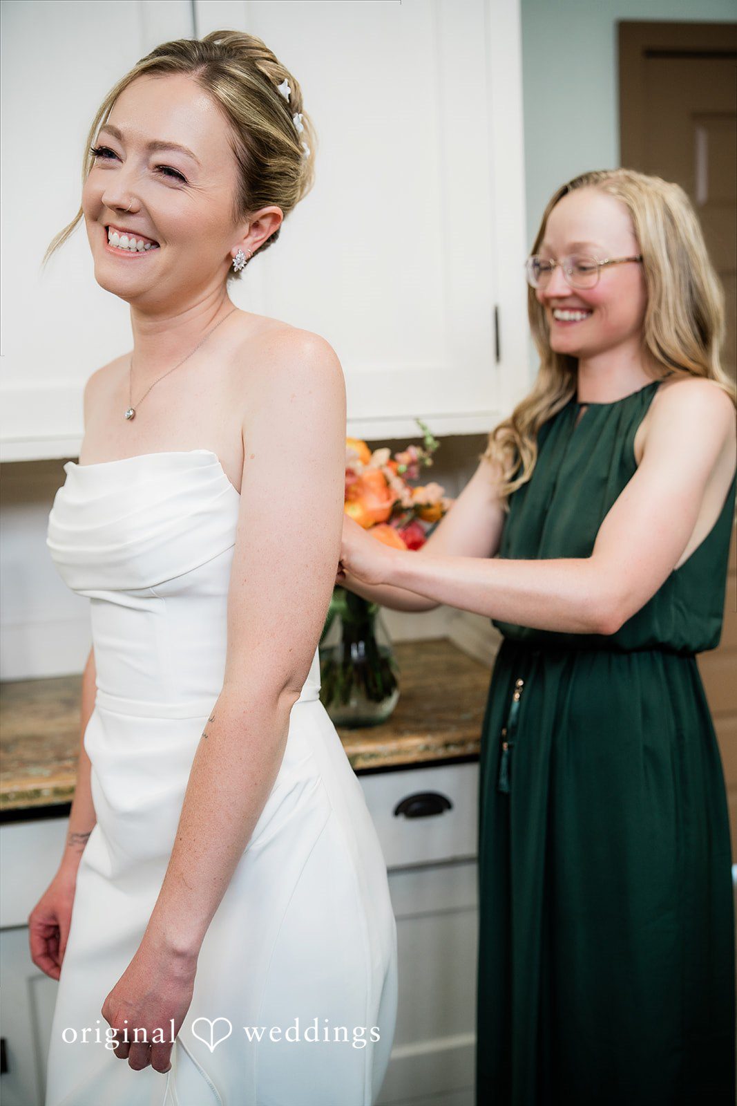 Sophia + Miles A woman helping a bride adjust the back of her white wedding dress.