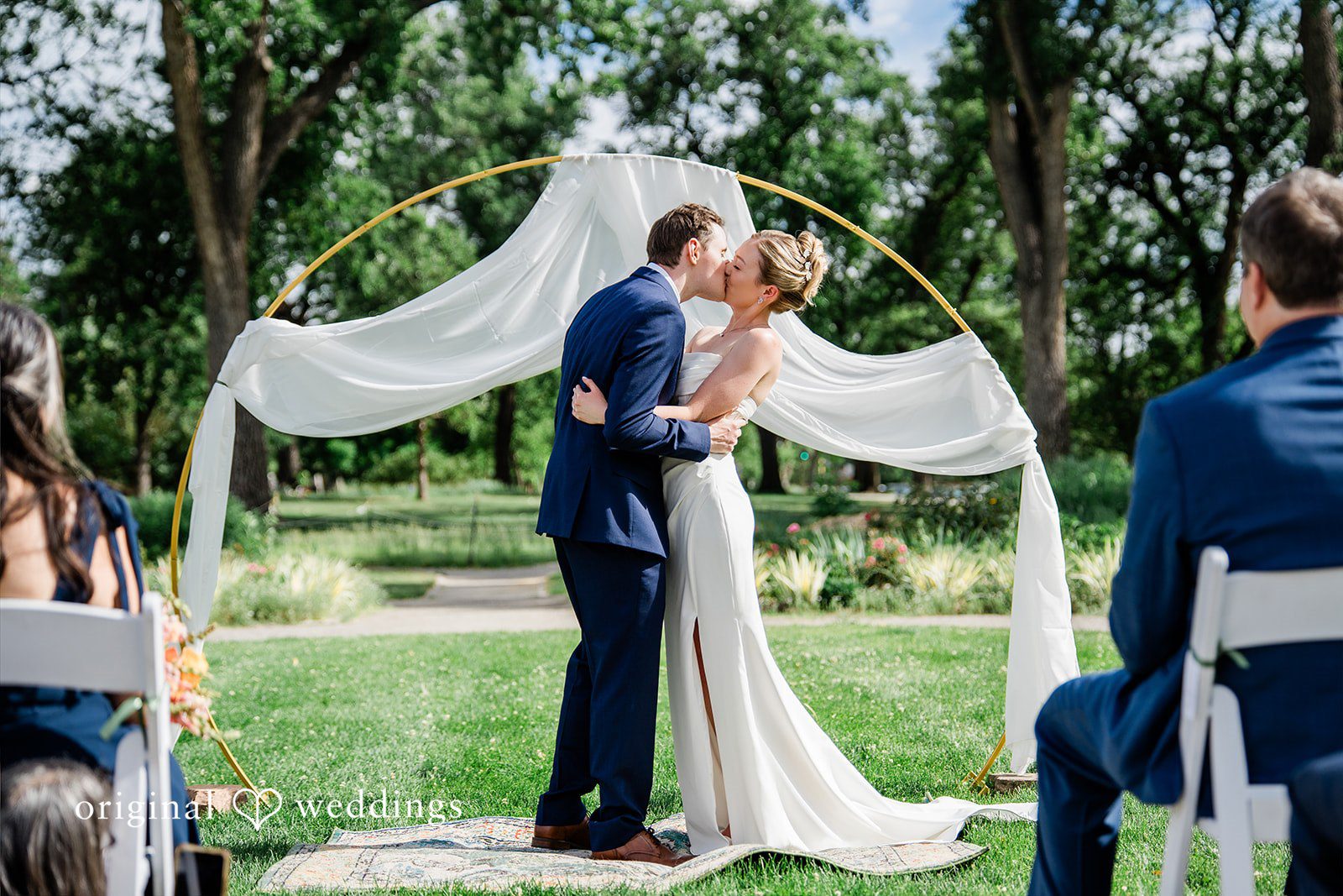 Sophia + Miles A bride and groom sharing a kiss under a white wedding arch.