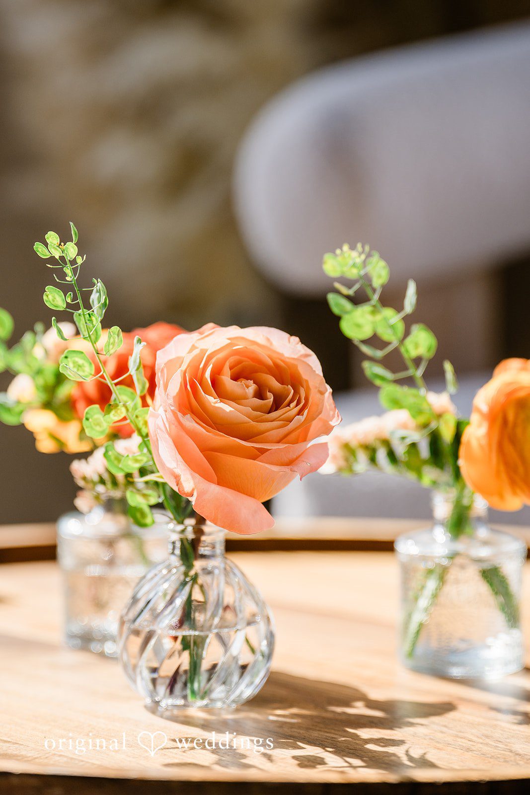 Sophia + Miles Close-up of bright orange roses in a small glass vase on a wooden tabletop.