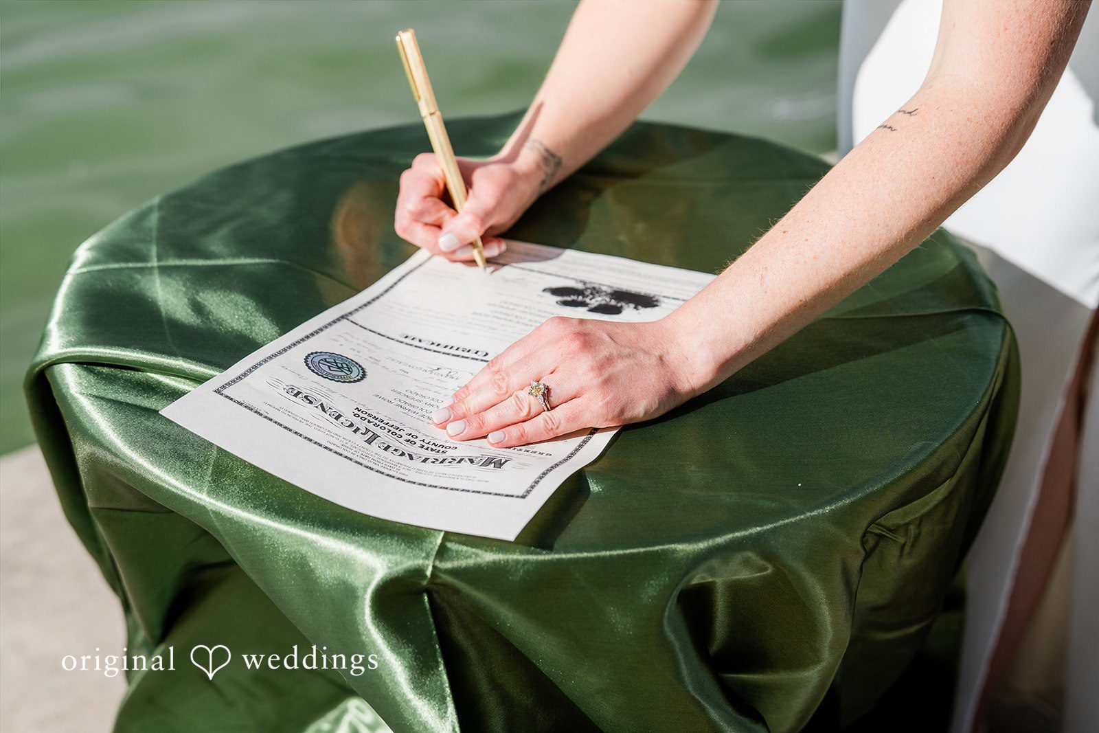 Sophia + Miles Bride signing a wedding document on a green velvet table cover.