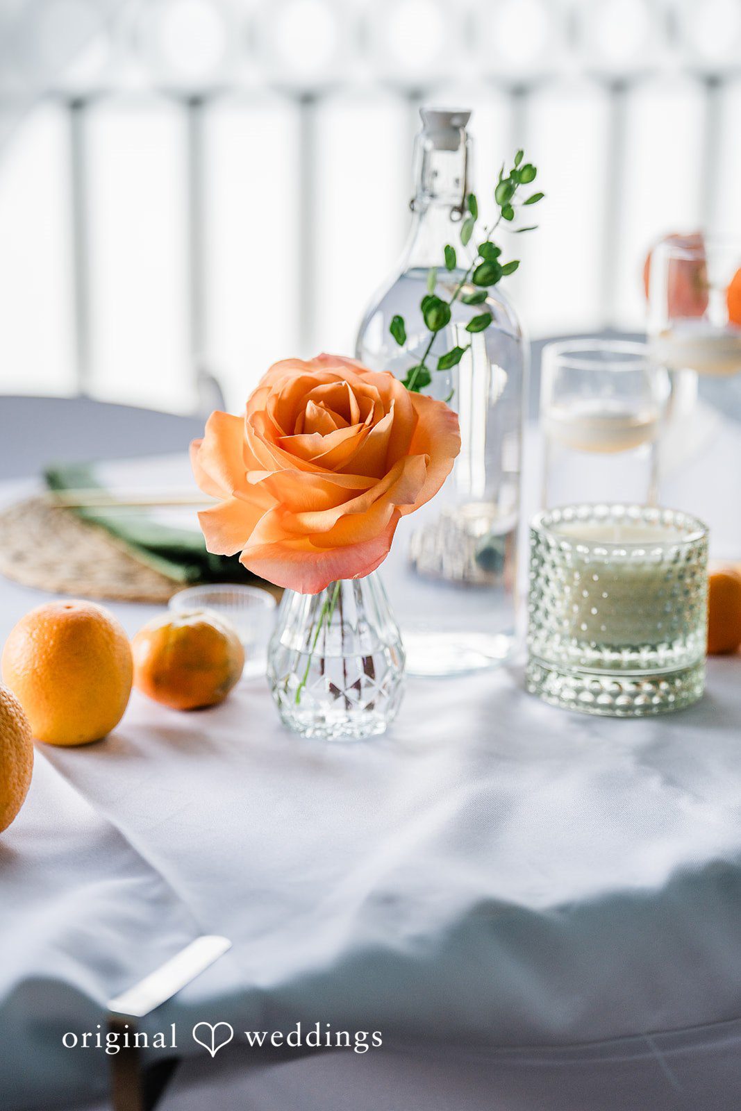 Sophia + Miles Table centerpiece arrangement with orange roses, white candles, and fresh whole oranges.
