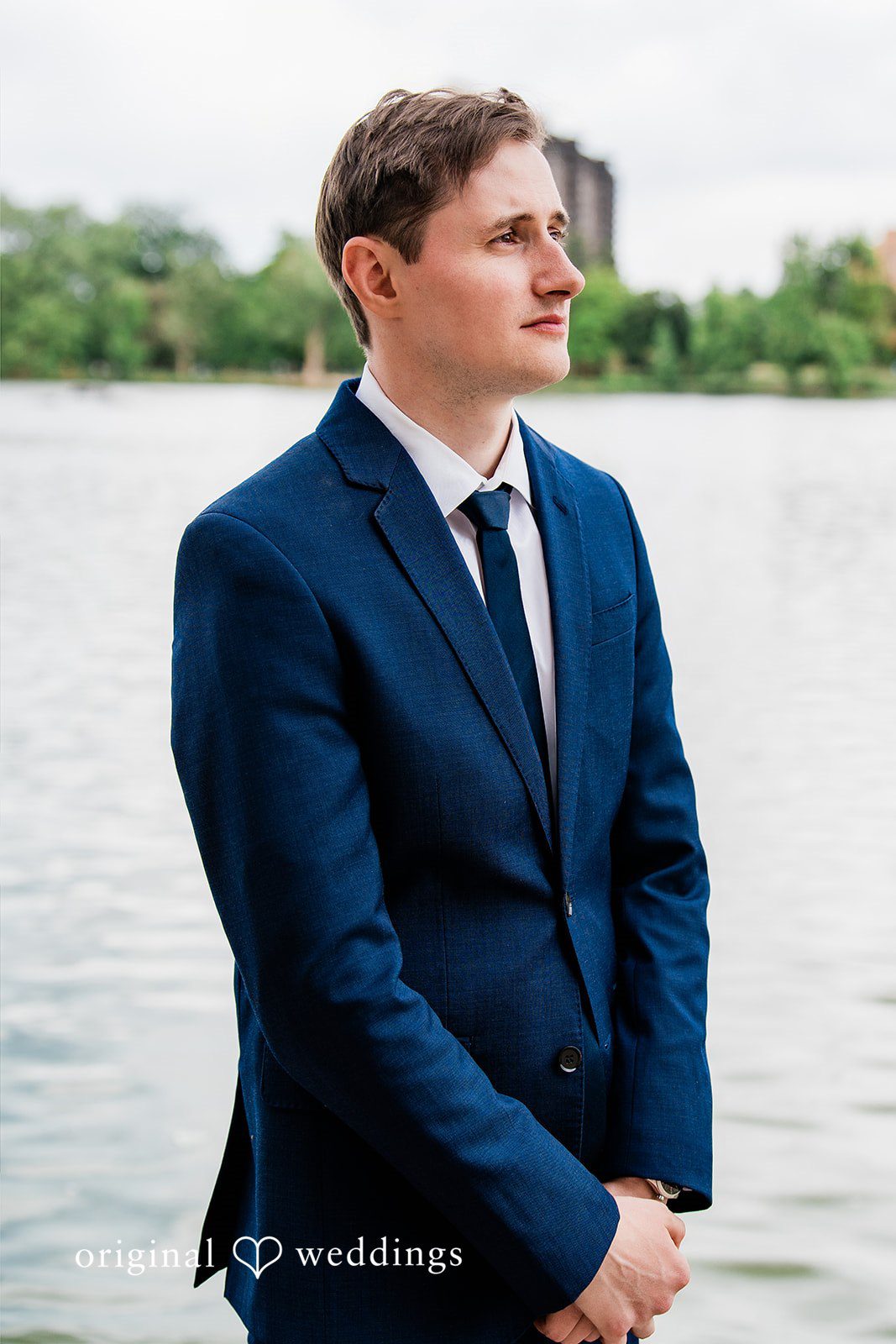 Sophia + Miles A groom in a navy blue suit standing alone with a body of water in the background.