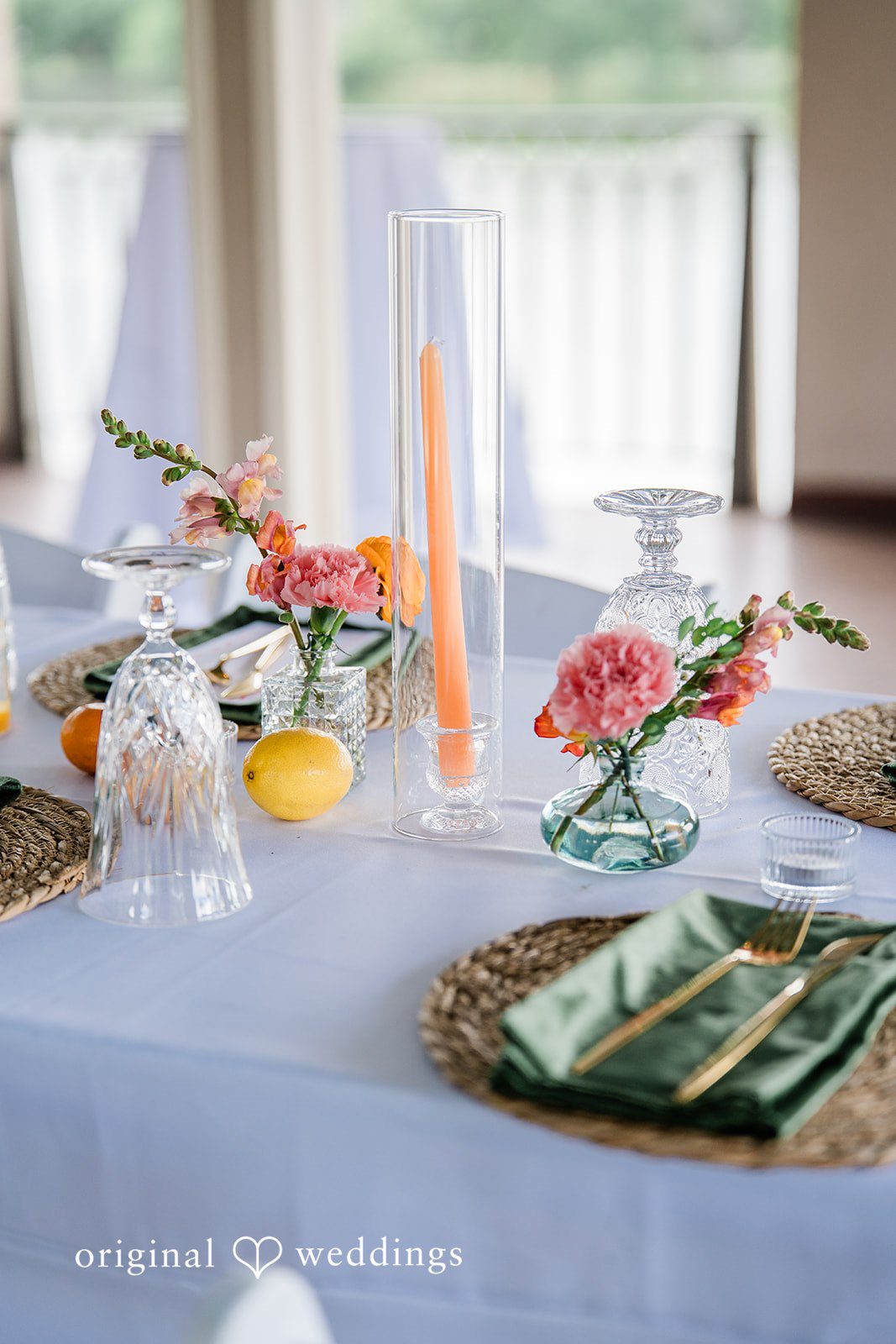 Sophia + Miles Table setting with light blue tablecloth, green cloth napkins, and glass vases with orange flowers.