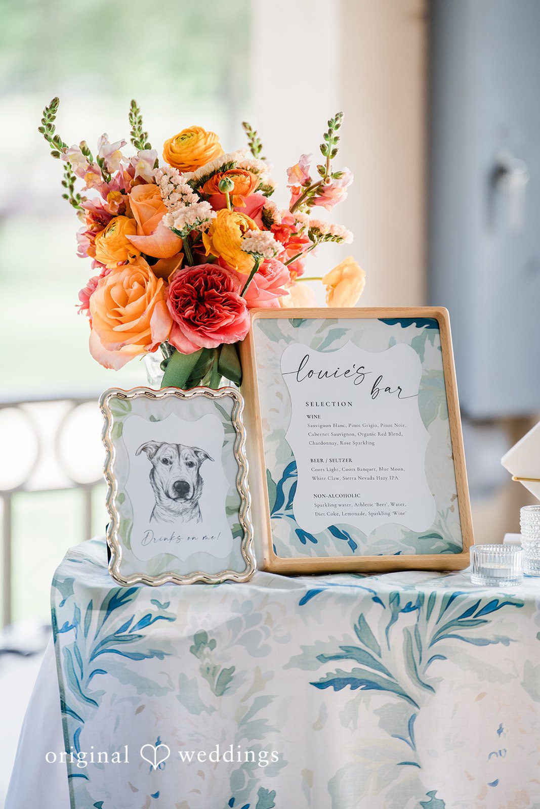 Sophia + Miles Wedding reception table details featuring a sign, patterned tablecloth, and orange floral centerpieces.
