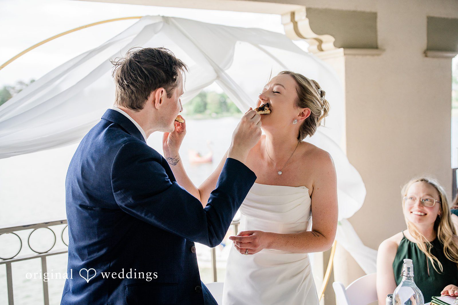 Sophia + Miles A groom feeding a piece of food to his laughing bride during their reception.