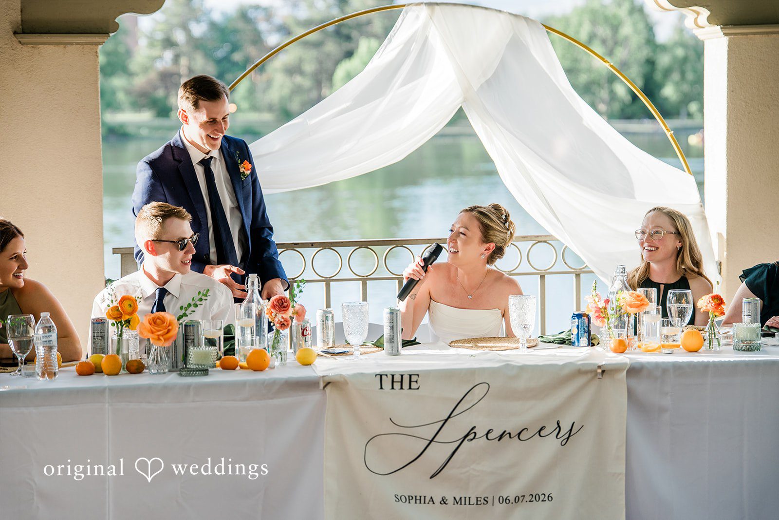 Sophia + Miles Guests and the wedding party seated along a decorated head table with white drapery in the background.