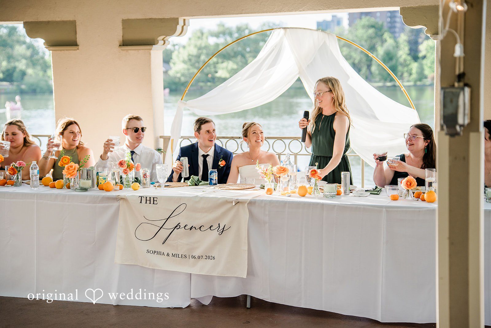 Sophia + Miles A wide view of the wedding party seated at a long banquet table under a white canopy.