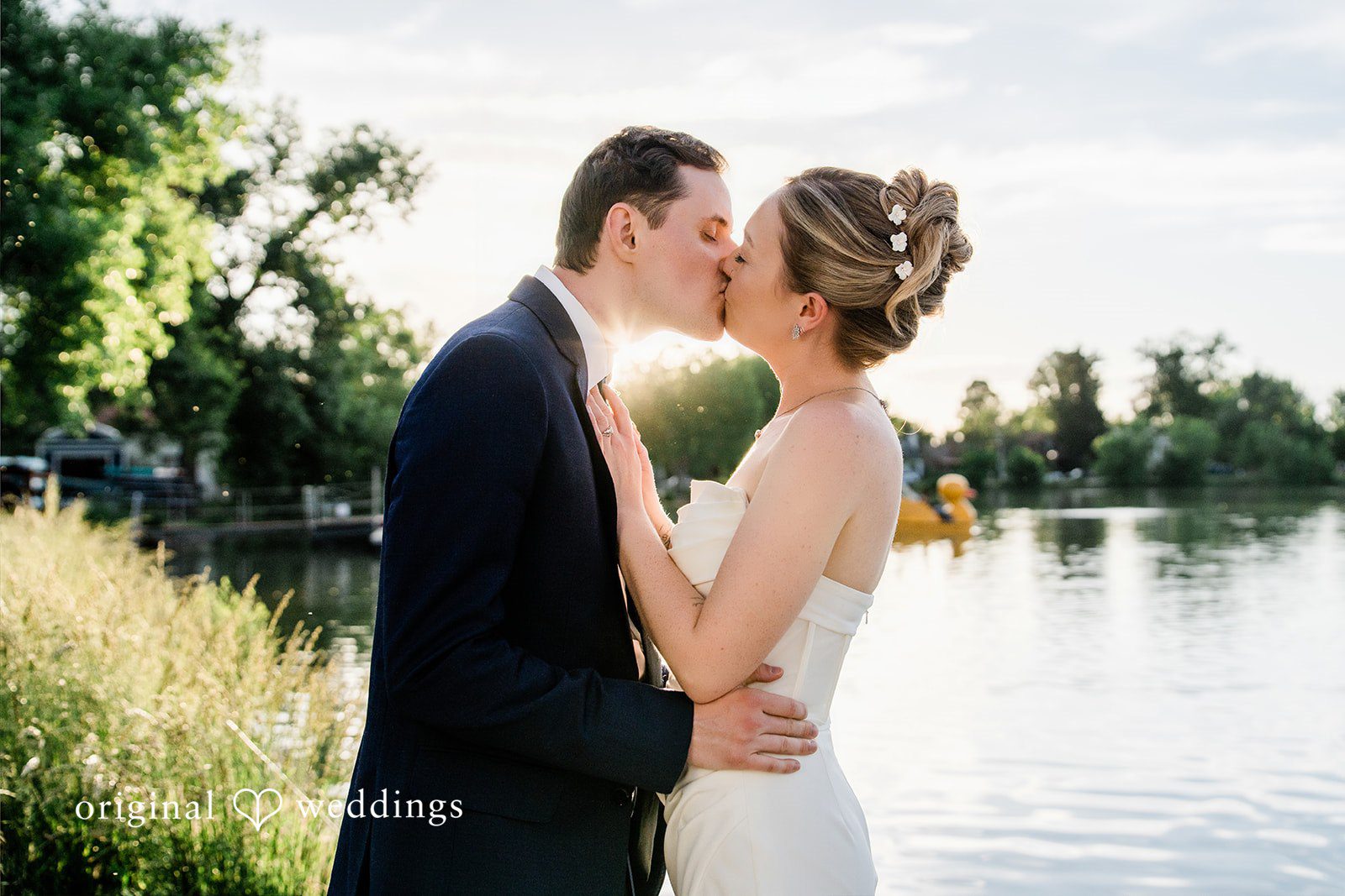 Sophia + Miles A bride and groom kissing tenderly on a waterfront pathway.