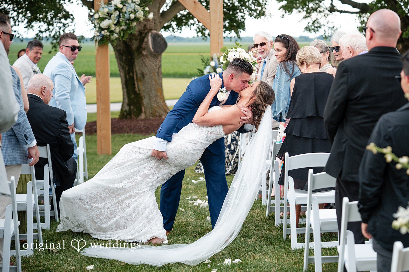 Newlyweds share a romantic dip kiss while guests applaud.