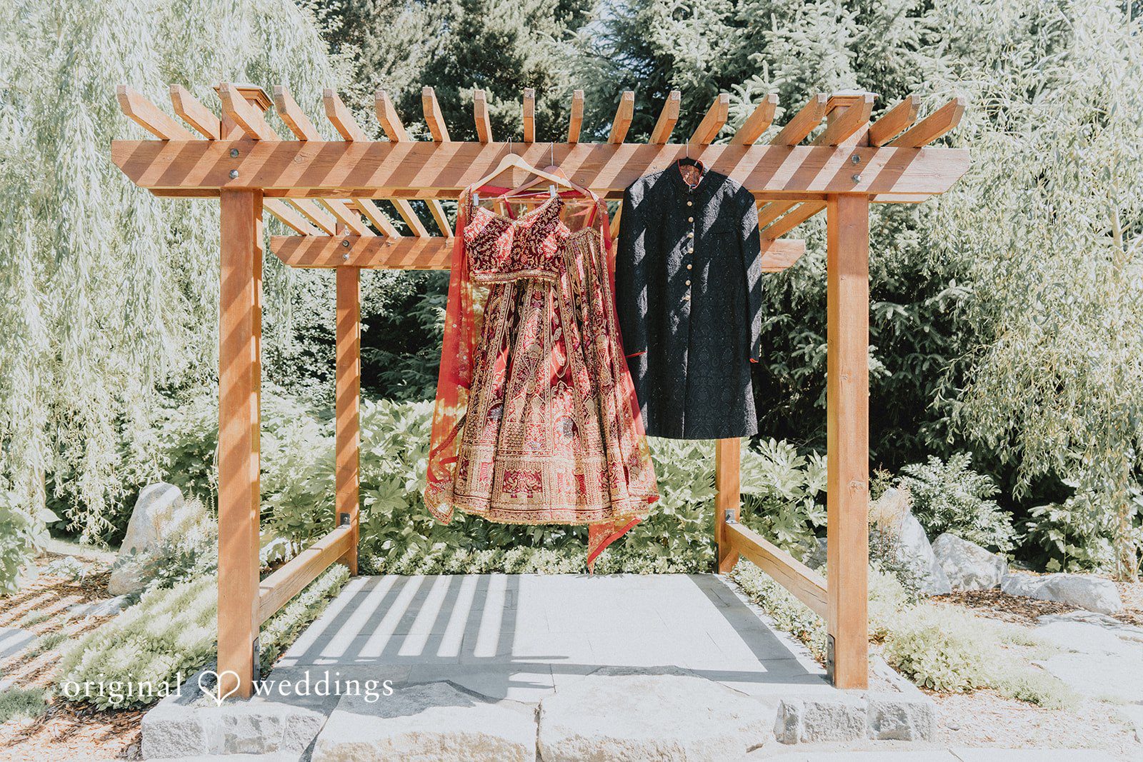 Traditional bridal lehenga and groom sherwani hanging beneath a wooden pergola at Willows Lodge