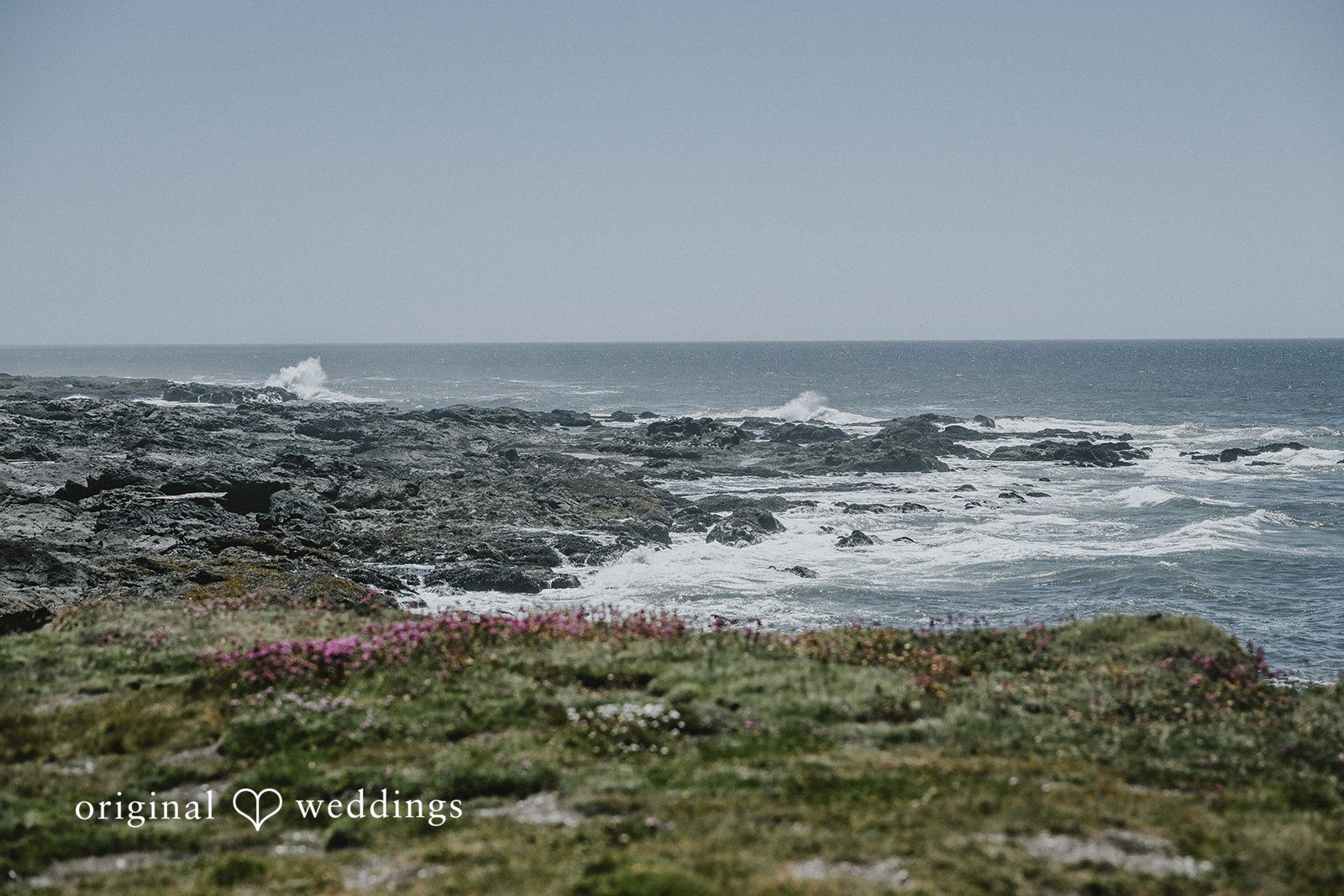 Rocky ocean coastline with crashing waves under an overcast sky.