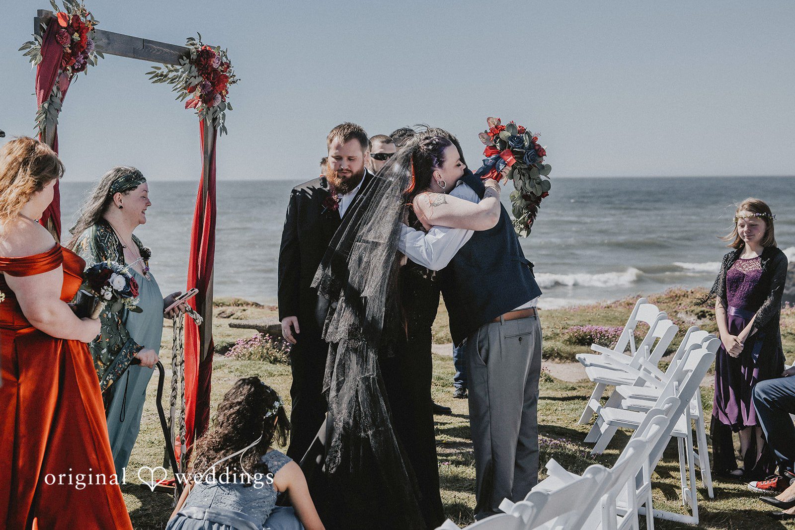 Wedding ceremony taking place by the ocean with guests watching.