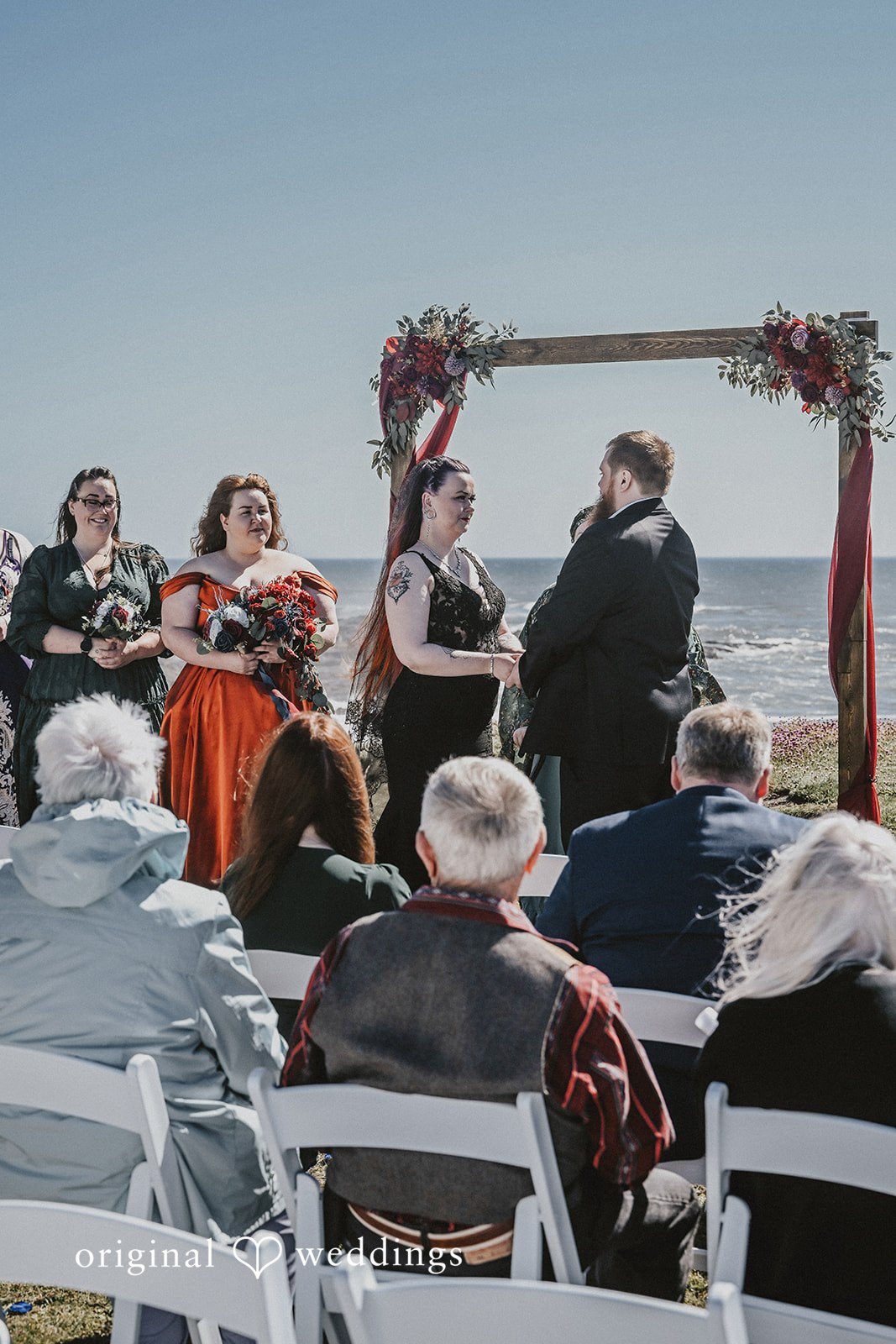 Wedding guests seated in rows watching an altar by the sea.