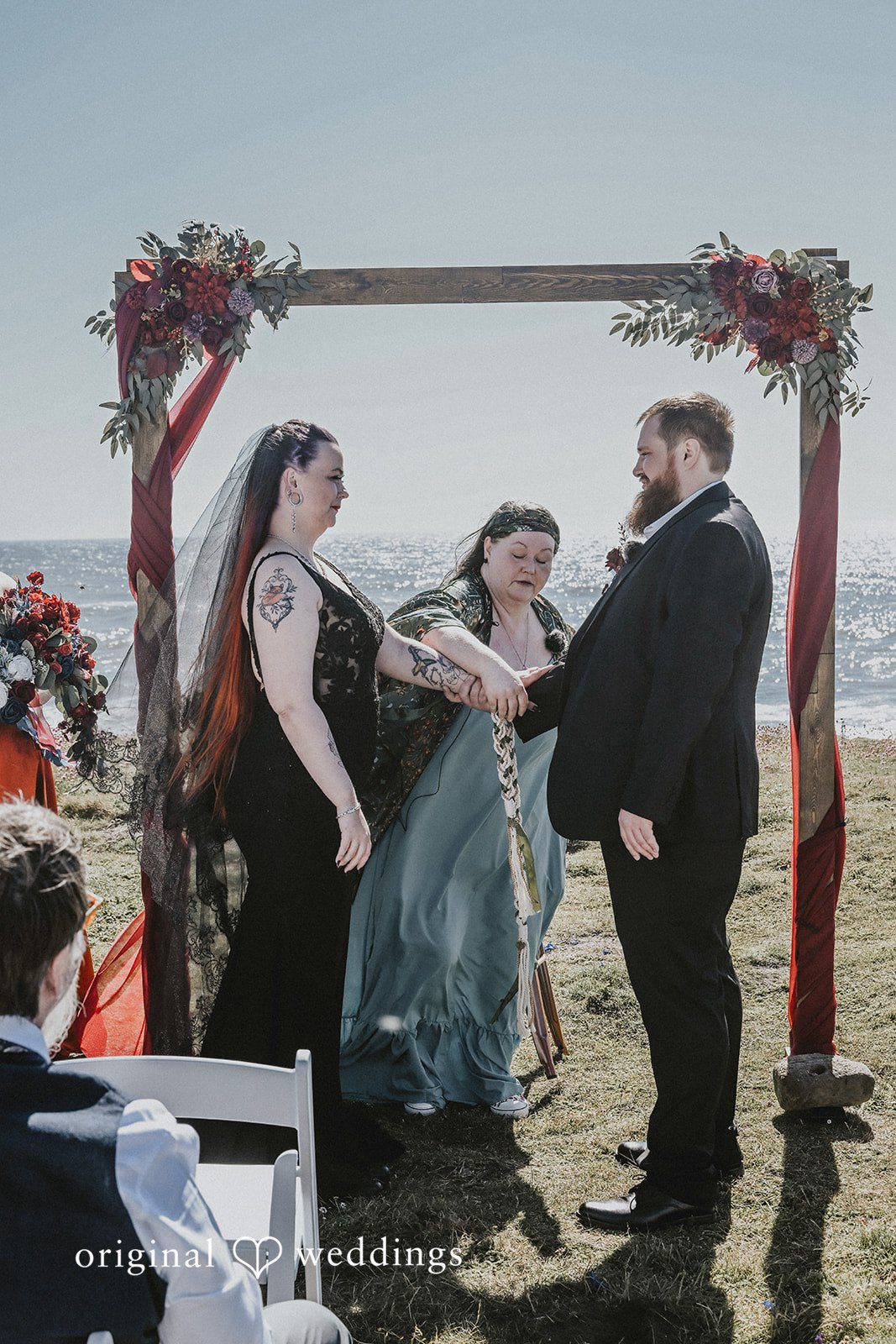 Bride and groom holding hands during their ceremony under a wooden arch.