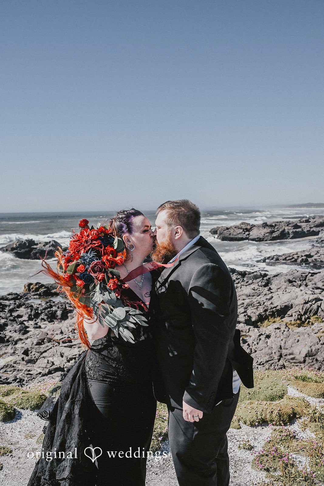 Bride and groom embracing and kissing against a rocky ocean backdrop.