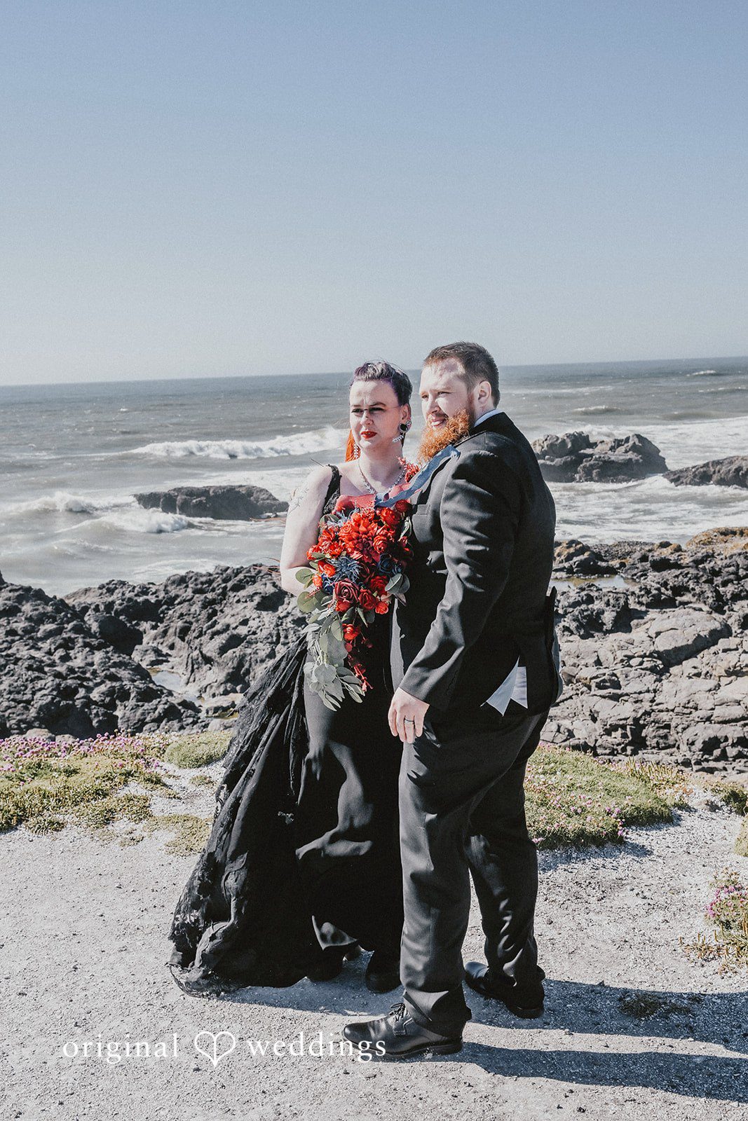 Bride and groom standing together on a rocky coastline.