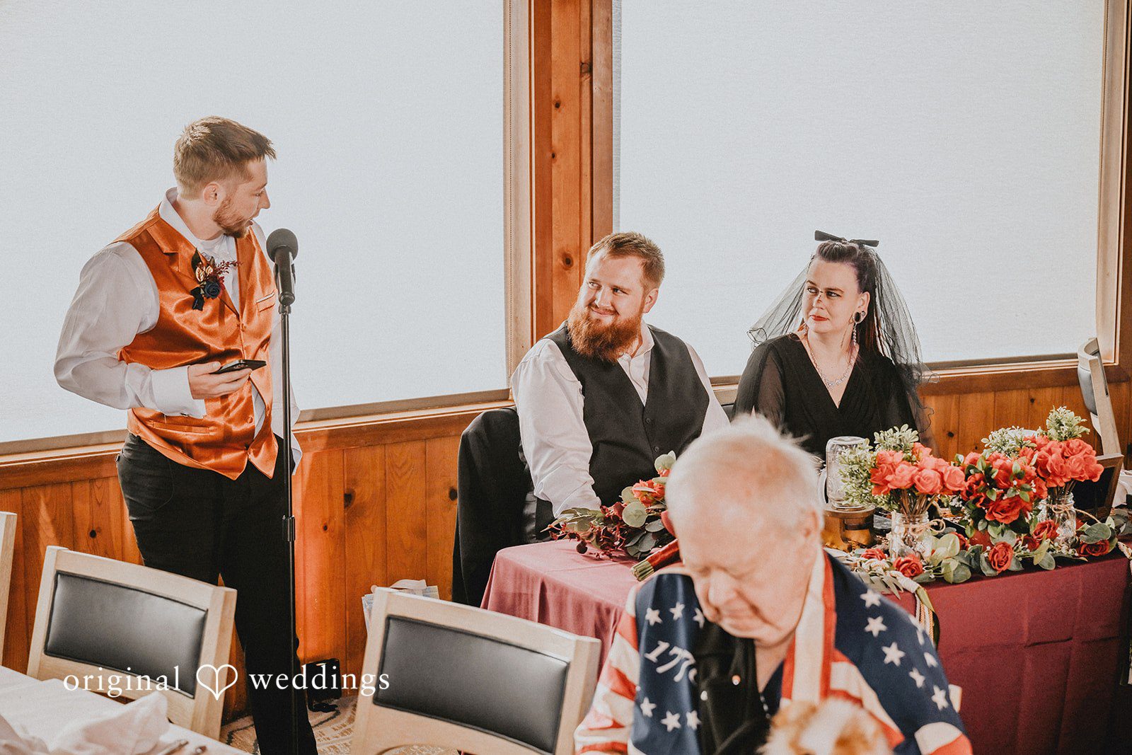 A man speaking into a microphone during wedding reception toasts.