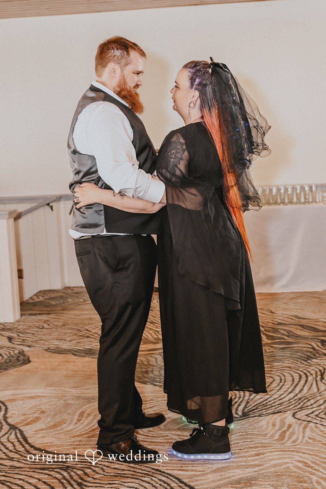 Newlyweds slow dancing closely together on a patterned reception floor.