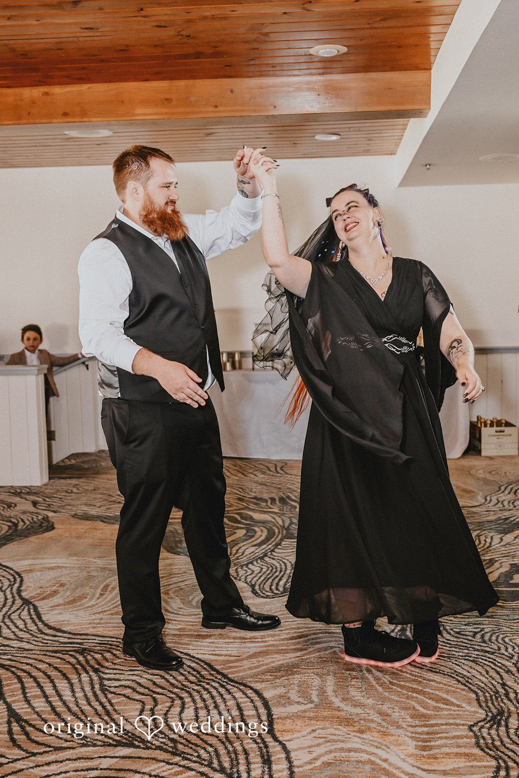 Groom and bride in a black dress smiling while dancing together.