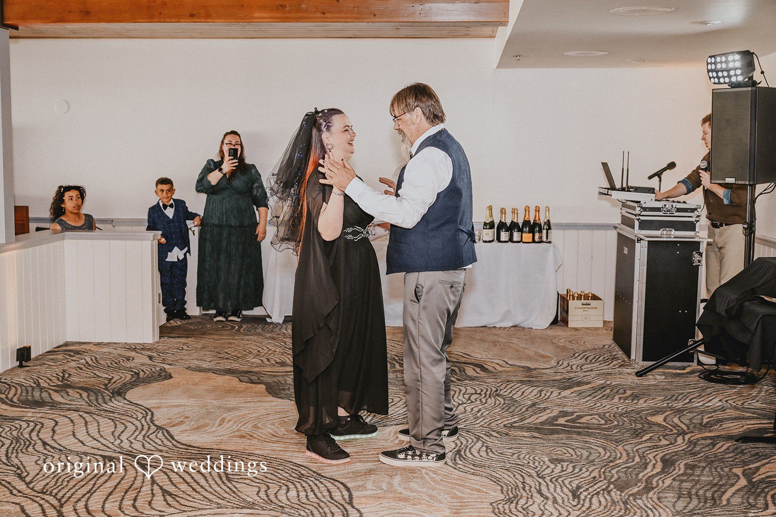 Bride in a black dress dancing with a man wearing a vest.