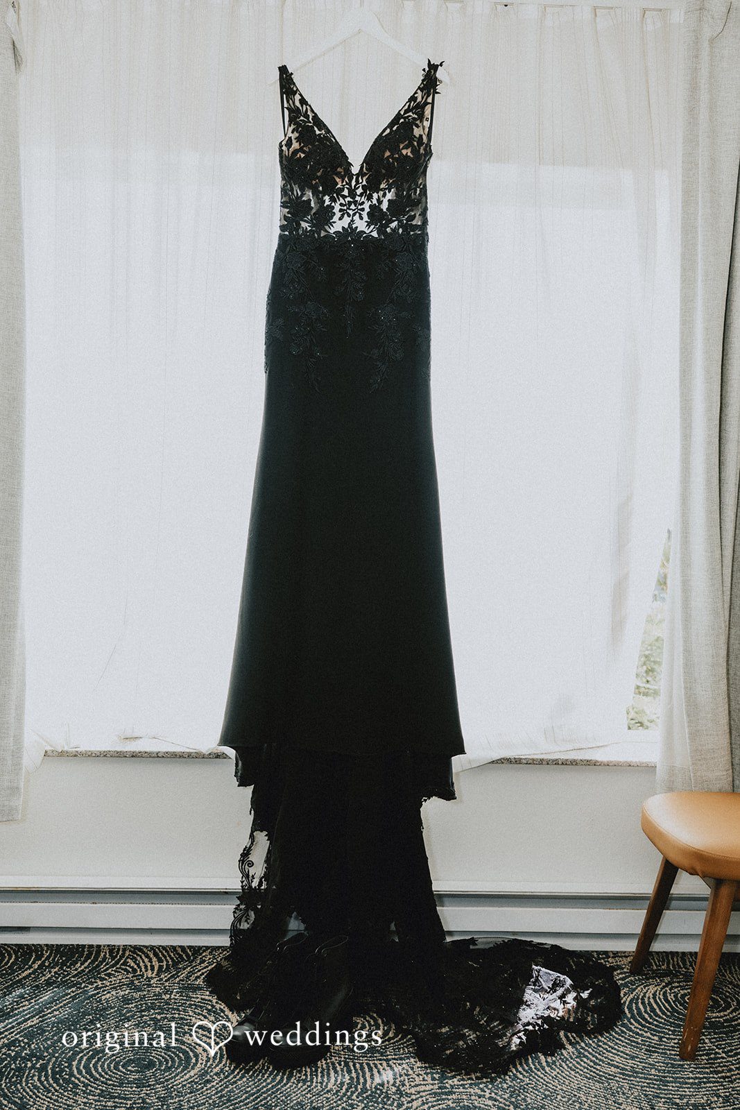 Elegant black wedding dress hanging against a white wall.