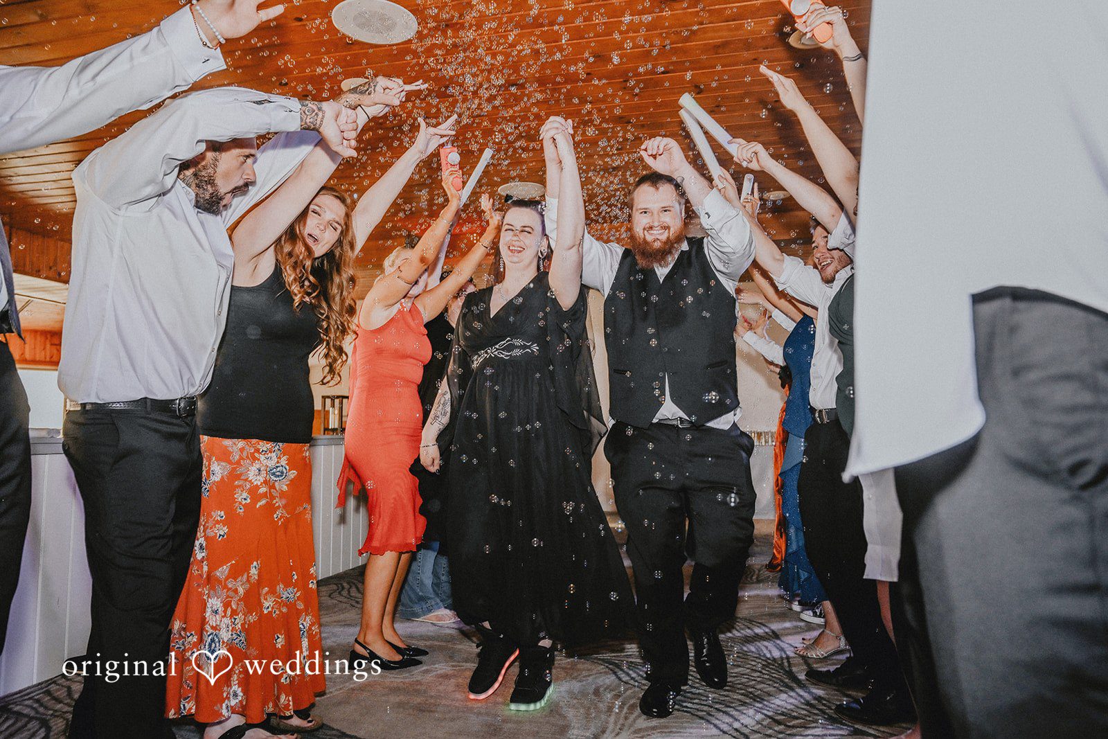 Wedding guests raising their hands together under a lit canopy structure.