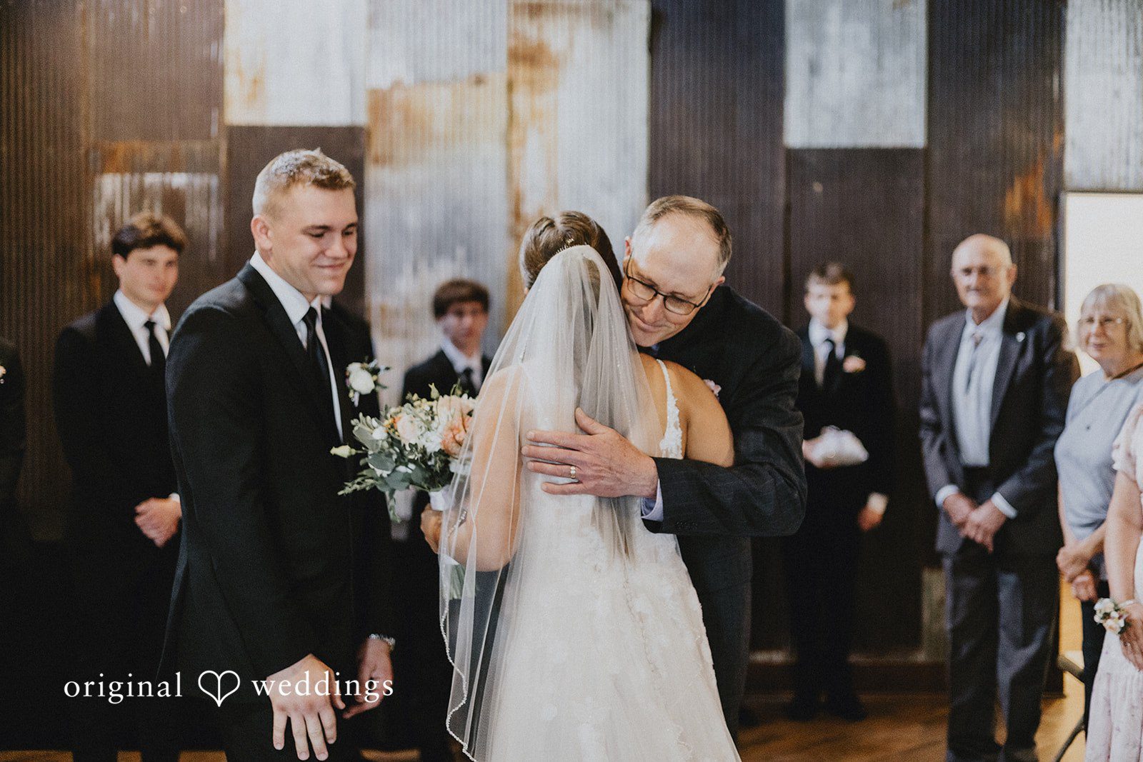 Emily + Ethan A man hugging the bride at the altar while the groom smiles nearby during the ceremony.