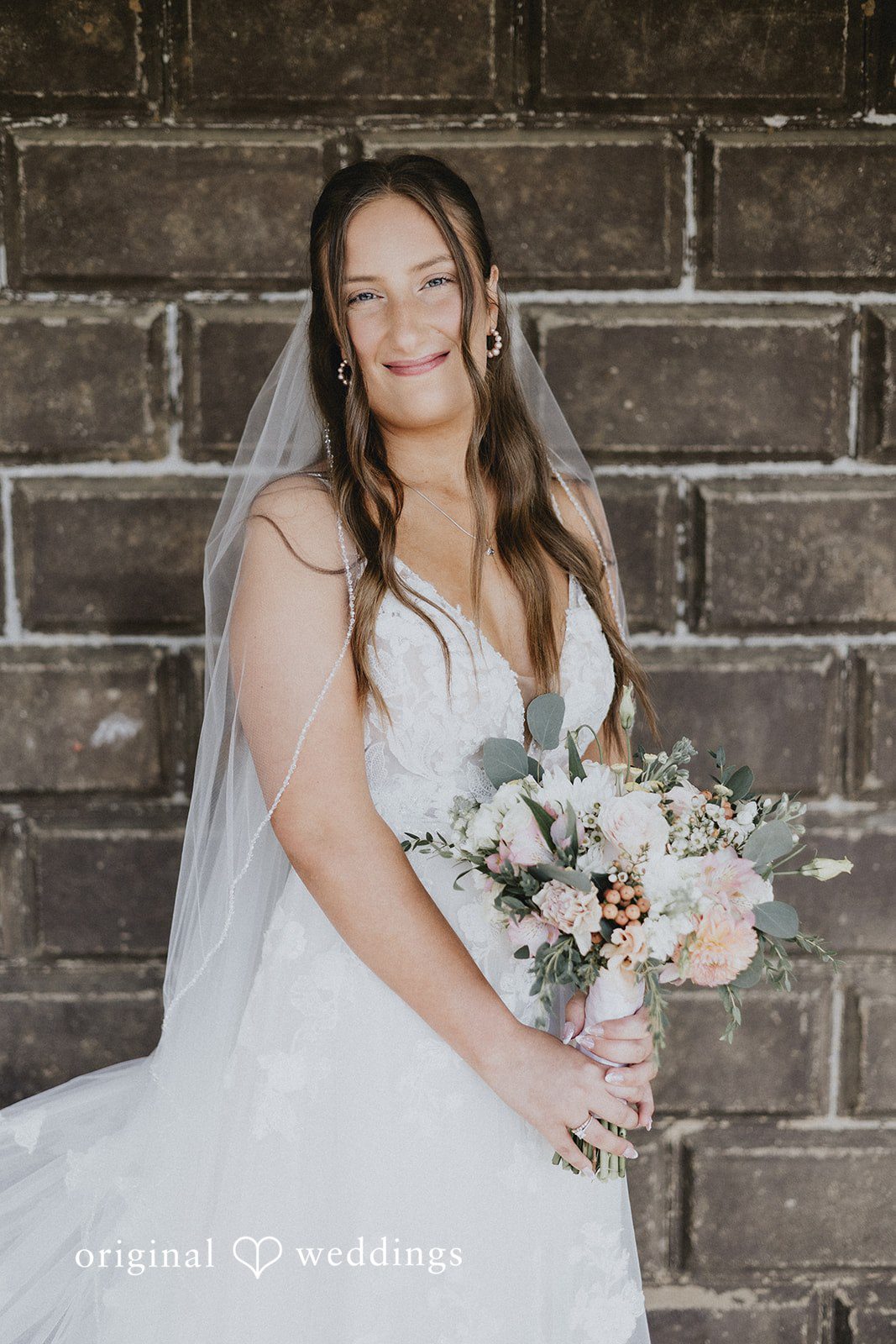 Emily + Ethan Bride holding a bouquet while posing against a stone wall.