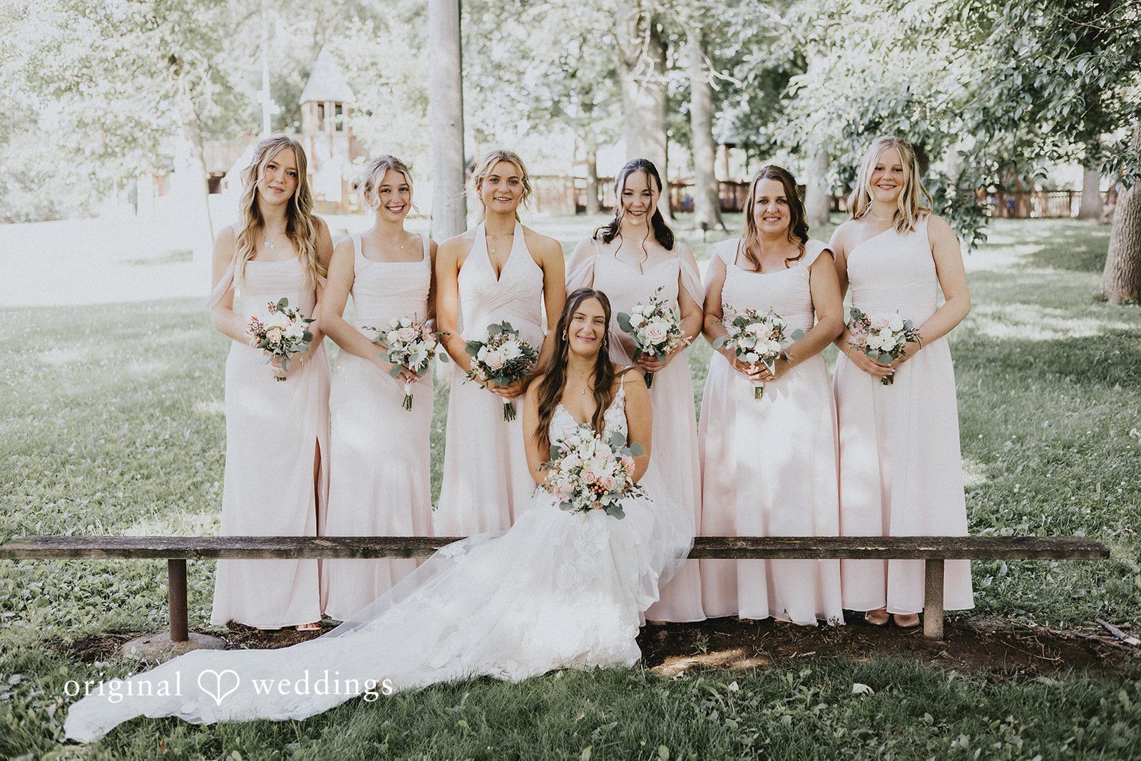 Emily + Ethan Bride and bridesmaids sitting together on a wooden bench.